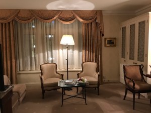 A view of the seating area in a "Deluxe King Room" at The Capital Hotel with a glowing standard lamp.