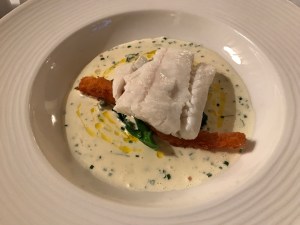 Fish dish consisting of a poached piece of white fish resting on a golden goujon in a creamy tartare sauce.
